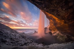 Colorful sunset in cave behind Seljalandsfoss waterfall in winter, Iceland