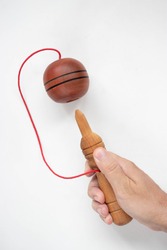 A hand holding a ball in a cup toy on a white background
