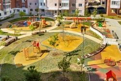 Top view of empty new modern children playground in courtyard of high-rise residential buildings in sunny summer day.