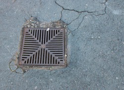 A square metal water drain grid set in cracked tarmac