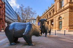 Bull and bear as a symbol figure. Place in front of the building of the Frankfurt Stock Exchange. Commercial buildings with a brown facade in the sunshine and blue sky with clouds 