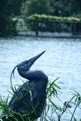 Heron sculpture in foreground, with lake and pergola in the background 