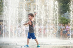 Excited boy having fun between water jets, in fountain. Summer in the city. Kid hit water with hand happy smile face. Ecology concept.