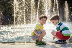 Cute toddler boy and older brothers, playing on a jet fountains with water splashing around, summertime concept