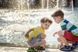 Cute toddler boy and older brother, playing on a jet fountains with water splashing around, summertime concept