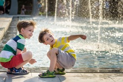 Cute toddler boy and older brothers, playing on a jet fountains with water splashing around, summertime concept