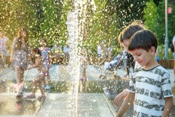 Boys jumping in water fountains. Children playing with a city fountain on hot summer day. Happy friends having fun in fountain. Summer weather. Friendship, lifestyle and vacation.