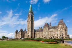 The Center Block and the Peace Tower in Parliament Hill, Ottawa, Canada. Center Block is home to the Parliament of Canada. The central green lawn and the red flowers  front the iconic building.