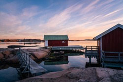 Two red boat houses with a small wooden bridge at sun rise in the Swedish archipelago on the west coast in Hunnebostrand. Bohuslän