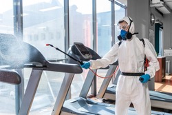 Cleaning and Disinfection in crowded places amid the coronavirus epidemic Gym cleaning and disinfection Infection prevention and control of epidemic. Protective suit and mask and spray bag
