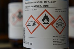 Chemical bottle with formic acid (acidum formicum) and three red labeled pictograms.