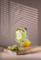  This is a fresh Mojito margarita cocktail with lime, lemon rosemary, mint and ice in a glass glass, a glass with a light background. Summer cold drink and cocktail