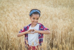 African American child smiling in love showing symbol and heart shape with hands. Portrait of beautiful African girl with a field of wheat on the background. Childhood, stop racism concept. Copy space