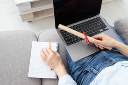 Female person with a diploma scroll sitting on the couch at home, holding a laptop on her lap. Concept for online student, distance learning, online university, secondary education, modern development