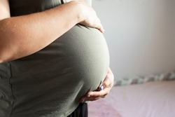 A pregnant woman home gently holds her round tummy with her hands. The concept of parenthood, 9 months of pregnancy, surrogate motherhood, expecting a baby, save pregnancy, maternity. Day light.