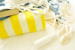 Concept of retreat, travel, vacation, summer, beach, good day, sun bathing, hotel, spa. On white bed lies striped yellow towel, bag with book, silk sundress, sunscreen and starfish. Nobody. Copy space