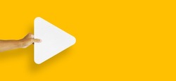 hand holding white paper media player button icon isolated on yellow background.