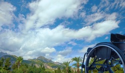 black wheelchair against the background of a bright cloudy sky, mountains and tropical vegetation, travel and recreation for people with disabilities concept 