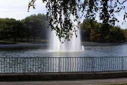 Fountain with pond into green city park with walking path 