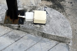 A white power connection box on the cement floor form a black metal stand.