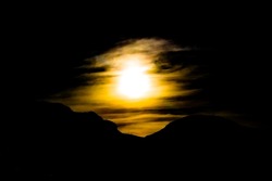 Hazy, yellow sun in dark sky over silhouetted mountainside