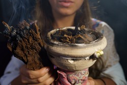 Hands of a spiritual woman holding burning tobacco and incense