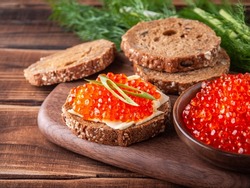 
Sandwich with red caviar on a wooden tray surrounded by bread, caviar and herbs, horizontal