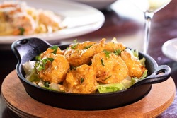 appetizer shareable starter small black round cast iron skillet wooden base creamy bang bang boom boom deep fried prawn shrimp seafood bed of lettuce rustic wooden dining table white wine glass