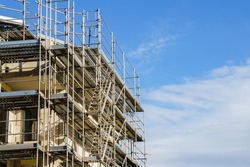 Frame of modern metal scaffolding with ladders on a building under construction on a background of blue sky.
