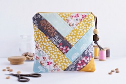 Quilted patchwork notions bag, glass jar with buttons, retro scissors and vintage wooden spools on white