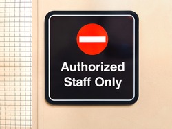 Close up of Authorized Staff Only sign on light yellow metal door with mesh wire pattern side window. 