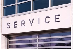 Selective focus of service sign at car dealer building entrance. Auto industry vehicle maintain, leasing, rental and services. Wholesale and logistic depot background.