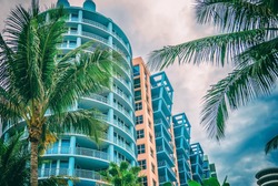 Architectural flat building Miami Style South Beach Florida image retro filtered 
Modern art deco condominium construction aqua and apricot color with palm trees against blue tropical sky background