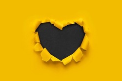 A paper hole with torn edges on a yellow background. Through paper. A ragged hole in the shape of a heart. Valentine's day. A symbol of love, romantic relationships. International Women's Day.