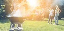 Food, people and family time concept - man cooking meat on barbecue grill at summer garden party