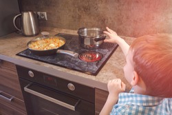 Child reaches for the hot electric stove. Child safety at the stove. 