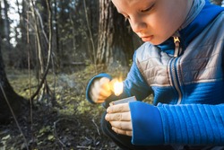 Selective focus. Little naughty boy sets fire to match in forest. Danger of child burns, attention. Careless handling of fire and flame, wildfire. Child holds burning torch in hands and plays