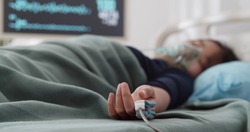 Teen asian girl in oxygen mask and oximeter sleeping in hospital bed. Portrait of unconscious child lying in bed and suffering from coronavirus in intensive care unit