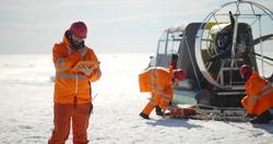 Coast guard team standing on frozen lake with hovercraft on background. Rescuers in safety uniform loading equipment in airboard preparing to patrol arctic area