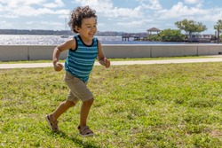 A young boy runs across the field while laughing out loud. The happy toddler is having a wonderful time running outdoors in the waterfront park.