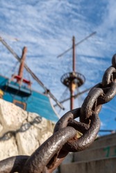 Strong chain link at the side of a dock harbour with ship in background strenght connection concept