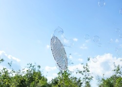 huge soap bubbles in the air against blue sky and green trees. summertime, having fun outside. copy space