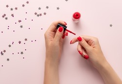 Woman applying red nail polish on her fingers. Manicure process. Beauty treatment and hand care concept. pink background with confetti