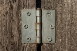Metal hinge on brown wooden planks with many screws in it.