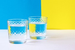 Two glasses with water on blue and yellow geometric background
