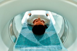 Portrait of a patient lying on CT or MRI, the bed moves inside the machine, scanning her body and brain. In a medical laboratory with high-tech equipment.