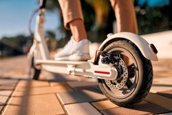 Close-up image of female feet on an electric scooter, with a wheel in the foreground.