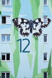 house detail of a modern apartment block, artistically designed with a mural pattern of polygonal shapes symbolizing abstracted floral elements and a painted checkered butterfly, Langen, Germany