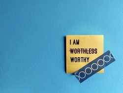 Note stick on copy space blue background with text I AM WORTHLESS change to I AM WORTHY, concept of self talk affirmation to overcome low self esteem, to love and accept value of oneself