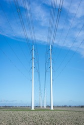 Row of modern high-voltage pylons with power lines for transporting electricity in the Dutch landscape